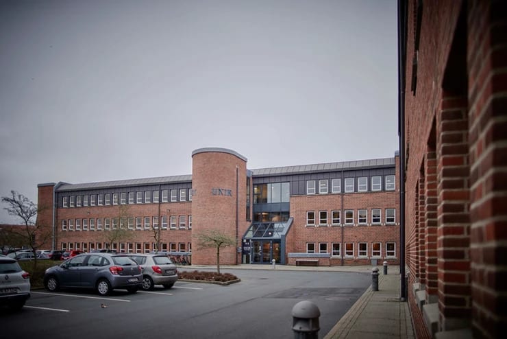 Providing property managers in Denmark a smarter way to run general meetings – Assembly Voting Unik System Designs Headquarters in Vejle, Denmark, which is a large red brick building with cars parked out front